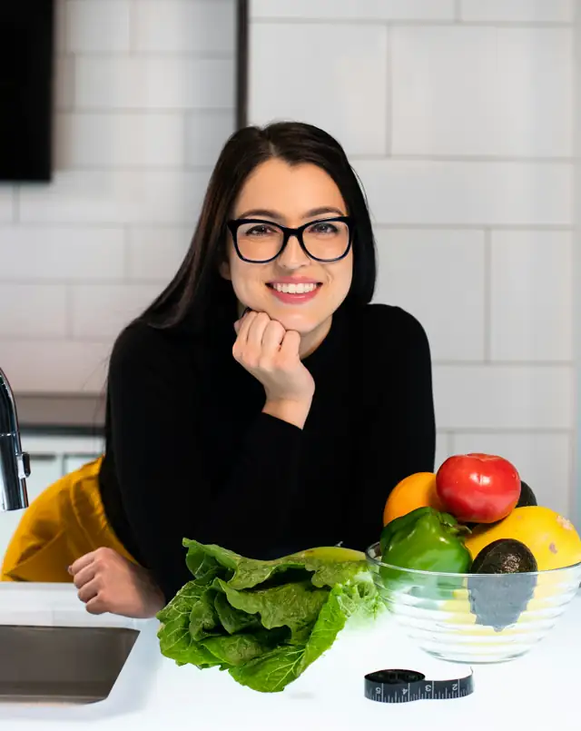 Nutricionista sorrindo, apoiada na mesa com frutas e verduras