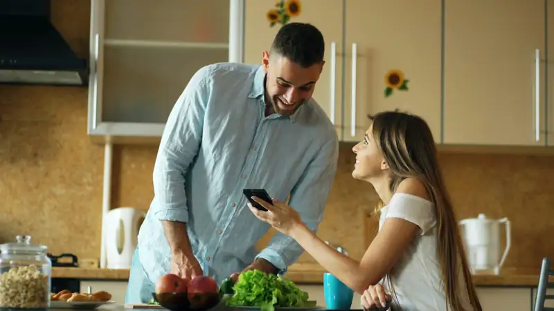 Casal na cozinha olhando o celular enquanto prepara uma refeição